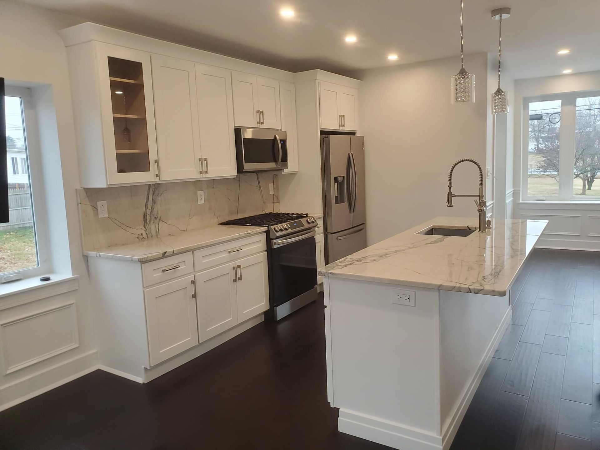 Bright modern kitchen with white cabinets, marble island, stainless appliances, and dark wood floors