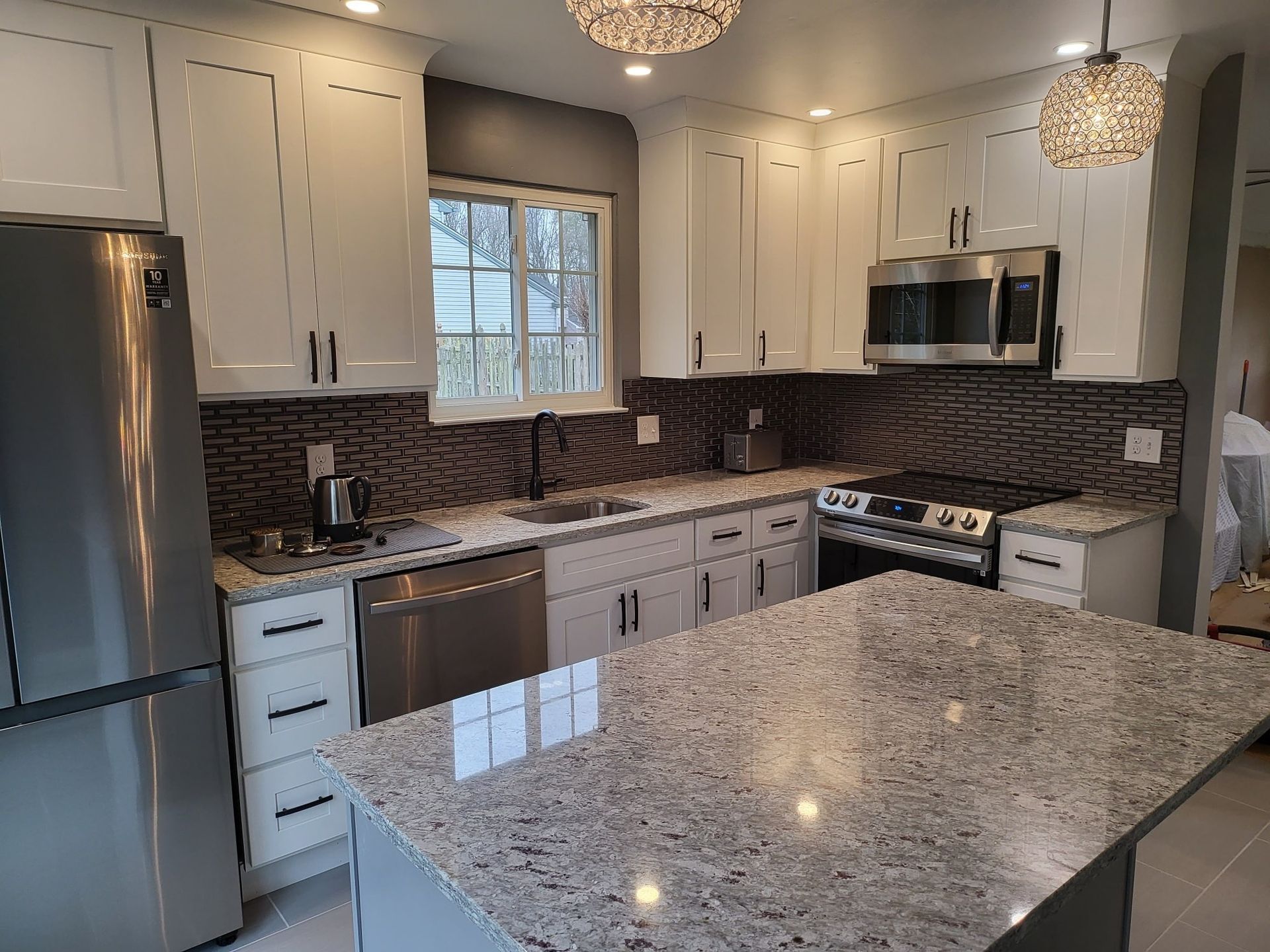 Modern kitchen with white cabinets, stainless appliances, dark backsplash, and a granite island countertop