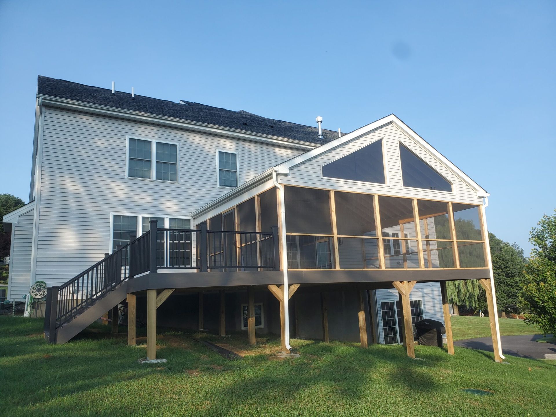 White house with a raised screened porch and deck on posts in a grassy yard, viewed from the side