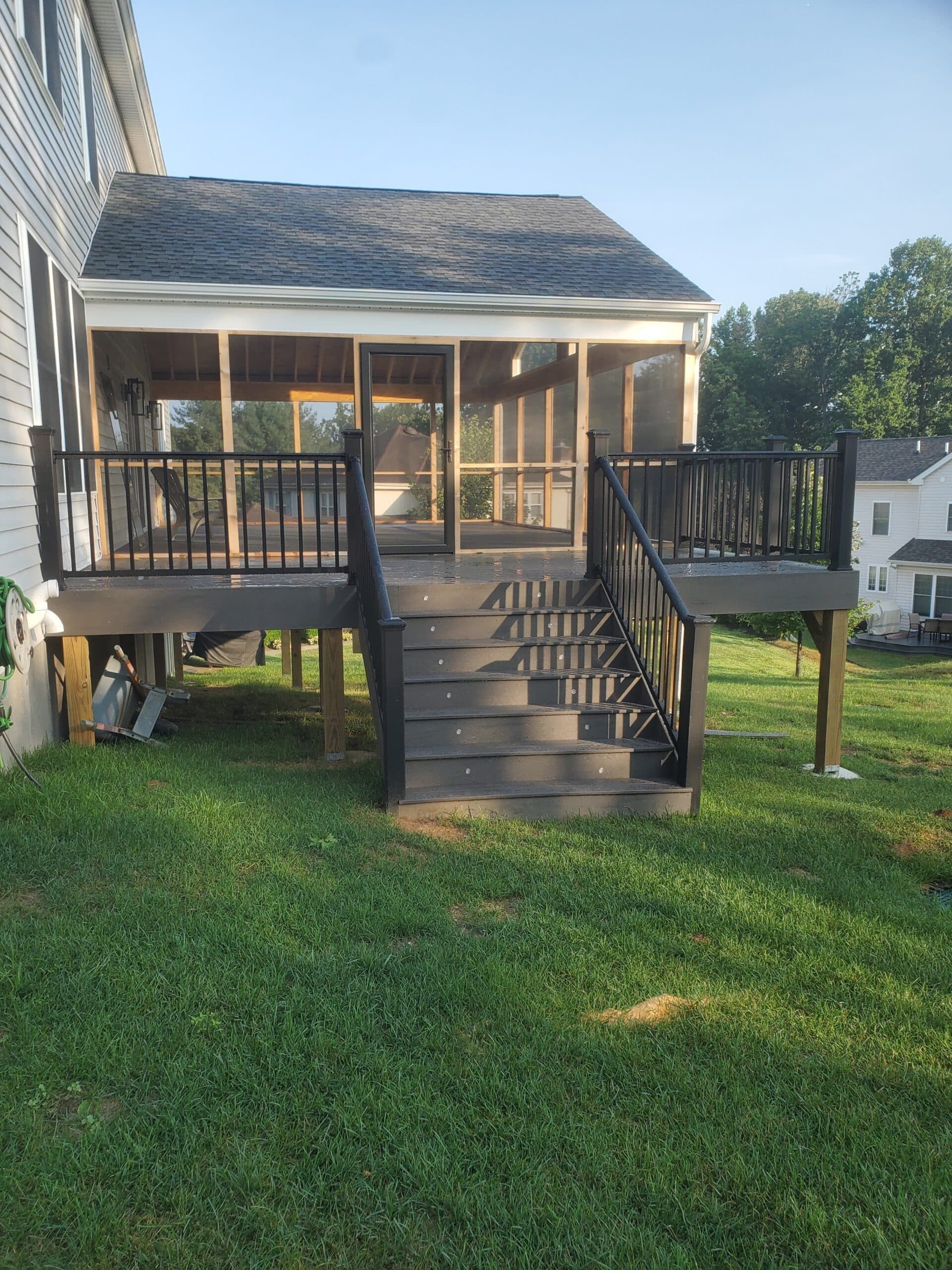 Backyard deck with central stairs, black railing, and screened porch beside a white house