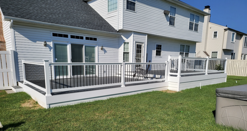 White house with a wooden deck and railing on a grassy lawn under a bright sky