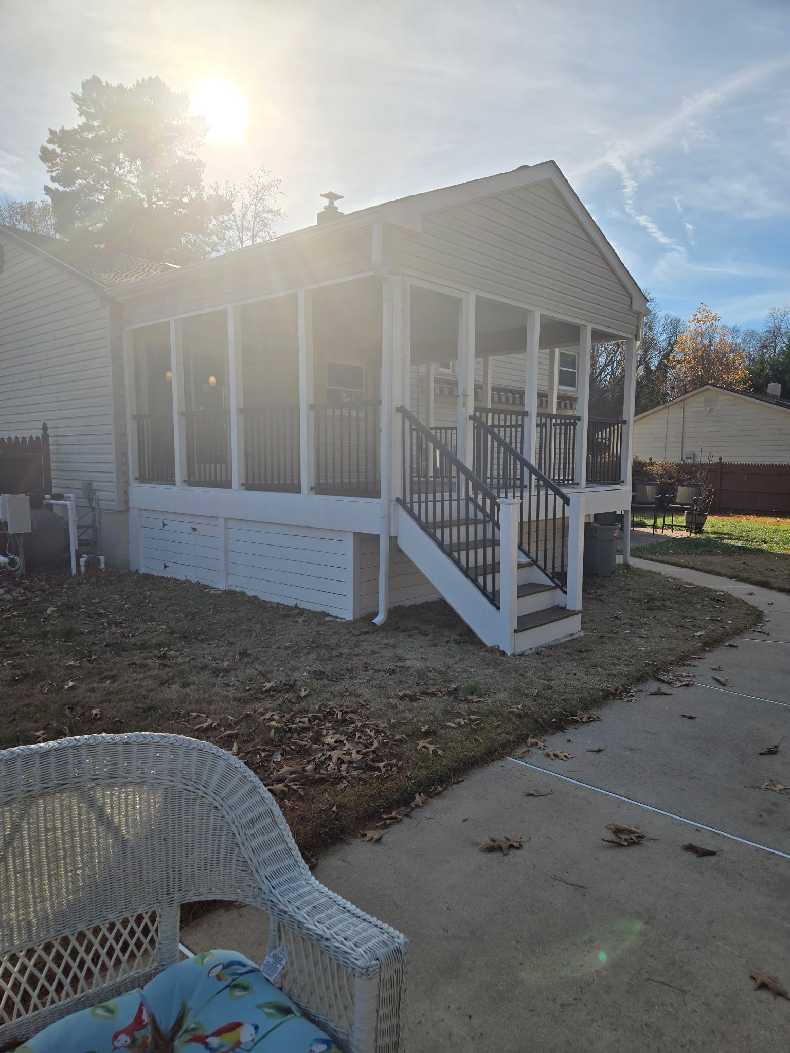 Small white screened porch with steps and railing beside a house in a sunny yard.