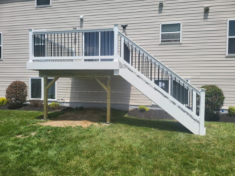 Elevated backyard deck with white railing and staircase beside a beige house