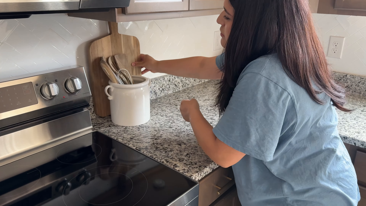 Person cooking at a stove, stirring a white pot in a bright kitchen.