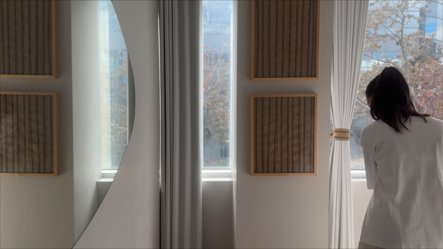 Person in a white shirt stands by a bright window in a sunlit room with woven wall panels.