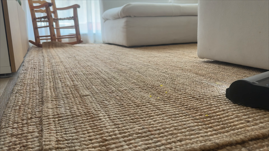 Low-angle view of a woven rug in a living room with white sofa, wooden chair, and black object on the floor