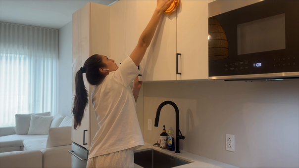 Person reaches up to a white kitchen cabinet beside a black microwave in a modern kitchen