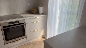 Modern white kitchen with built-in oven, drawers, countertop decor, and bright window light