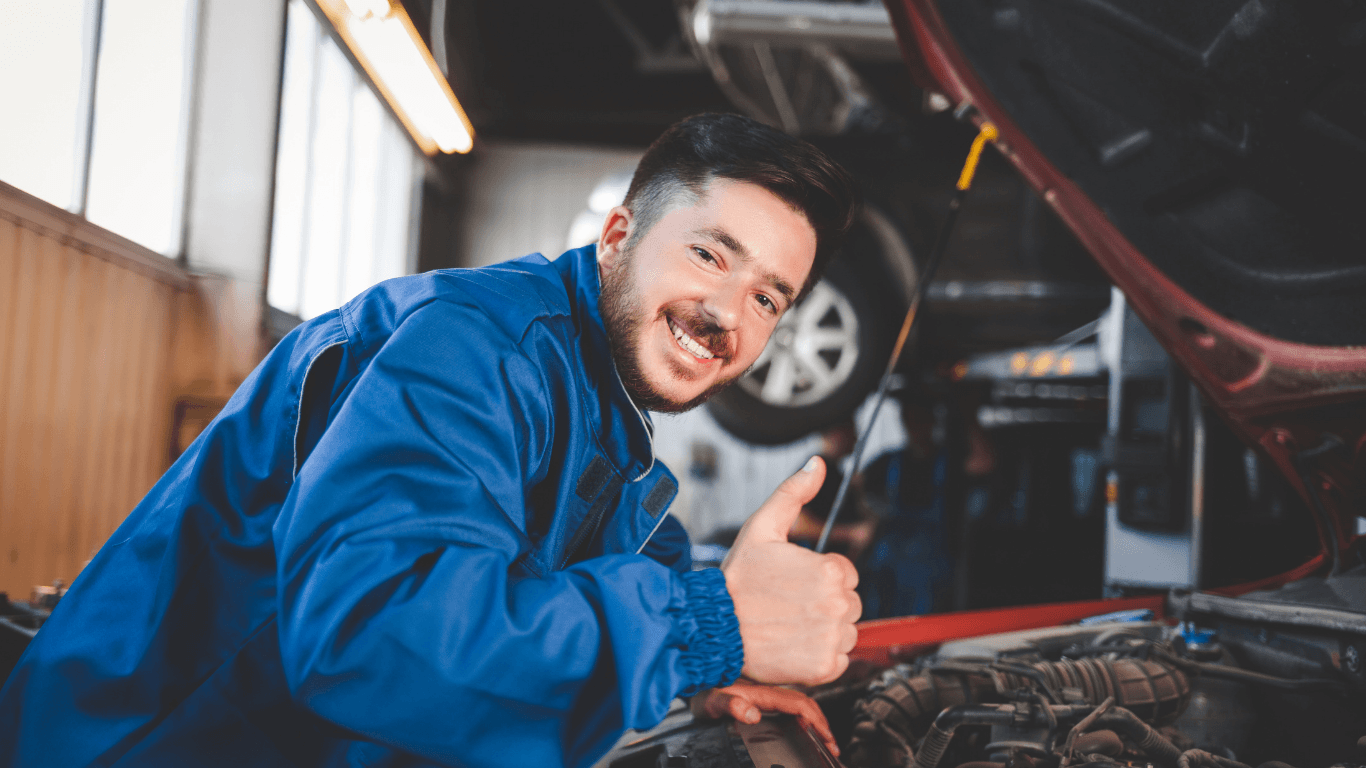A mechanic smiling under the hood of a red car