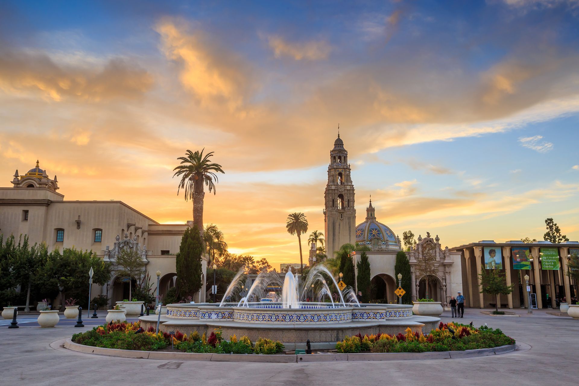 A fountain in a circle in front of a building at sunset.