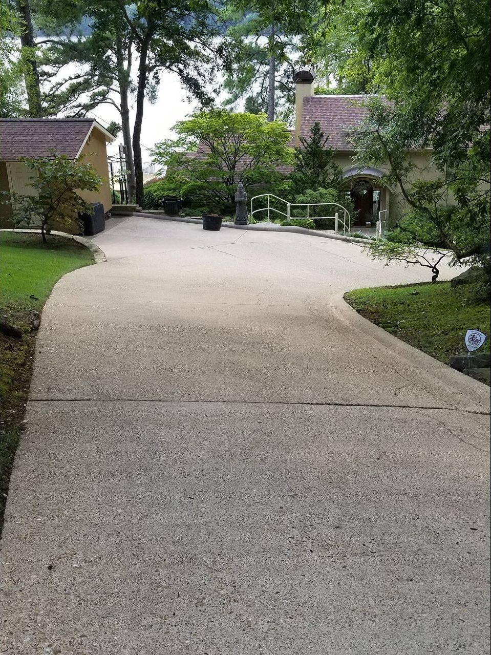 A concrete driveway leading to a house surrounded by trees.
