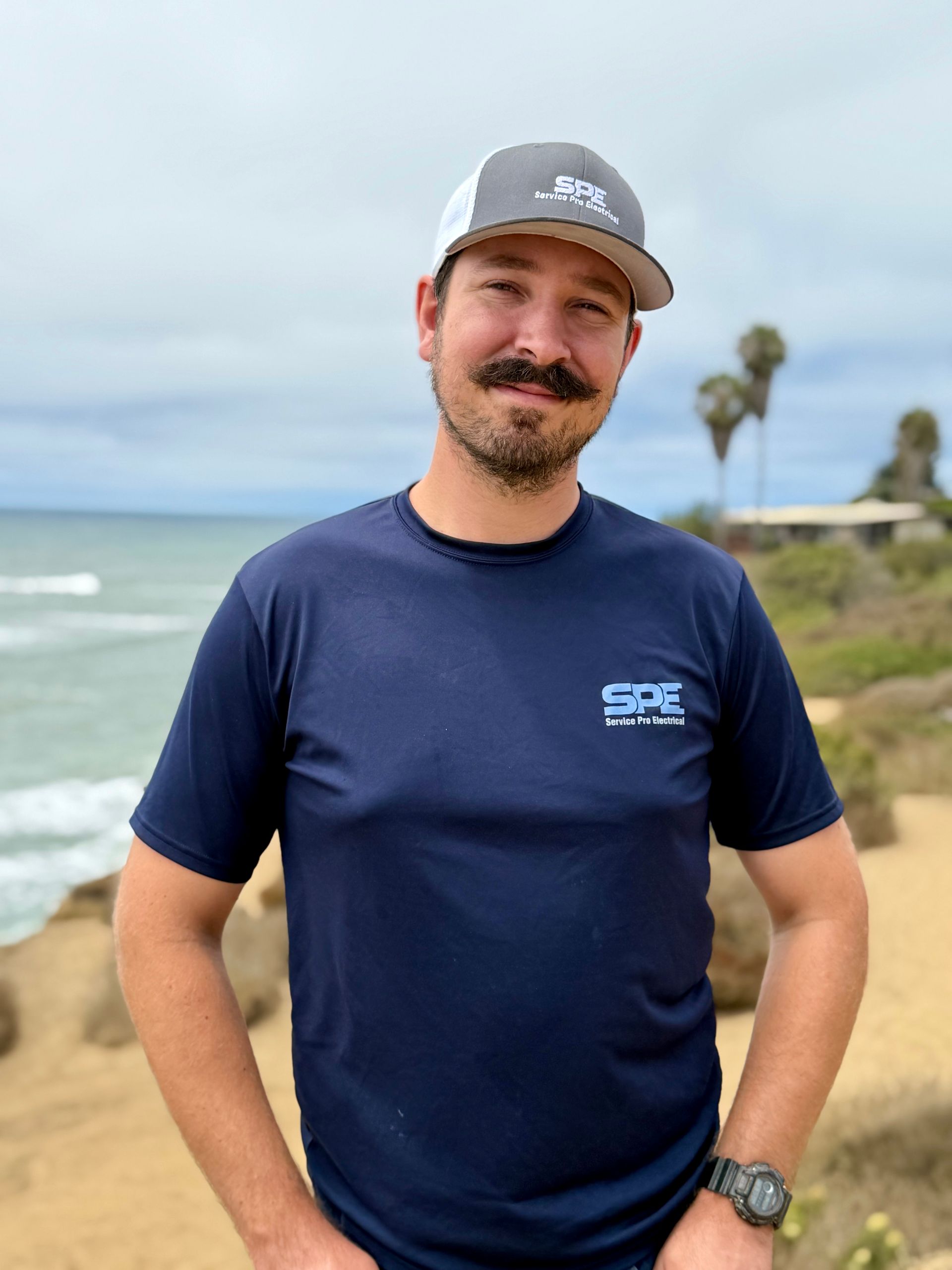 A man with a mustache is standing on a cliff overlooking the ocean.