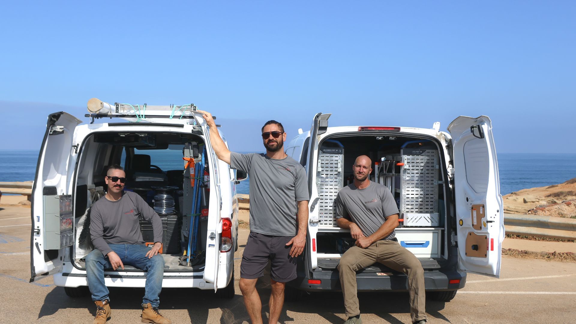 Three men are standing in front of two vans.