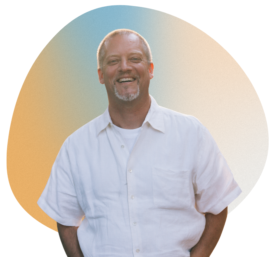 Man with a short gray beard smiles, wearing a white shirt, in front of an orange-blue gradient backdrop.