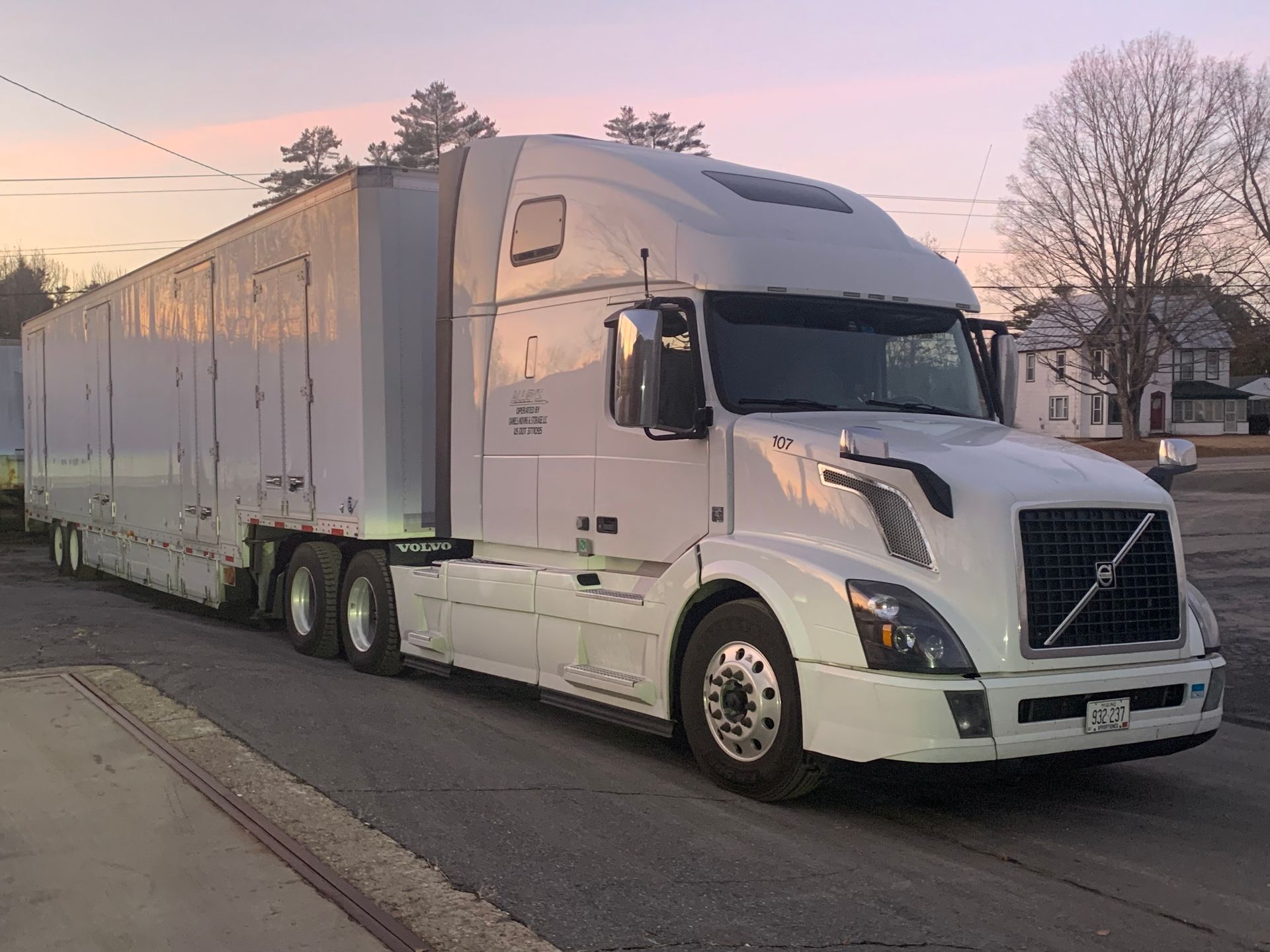 A white semi truck with a trailer attached to it is parked on the side of the road.