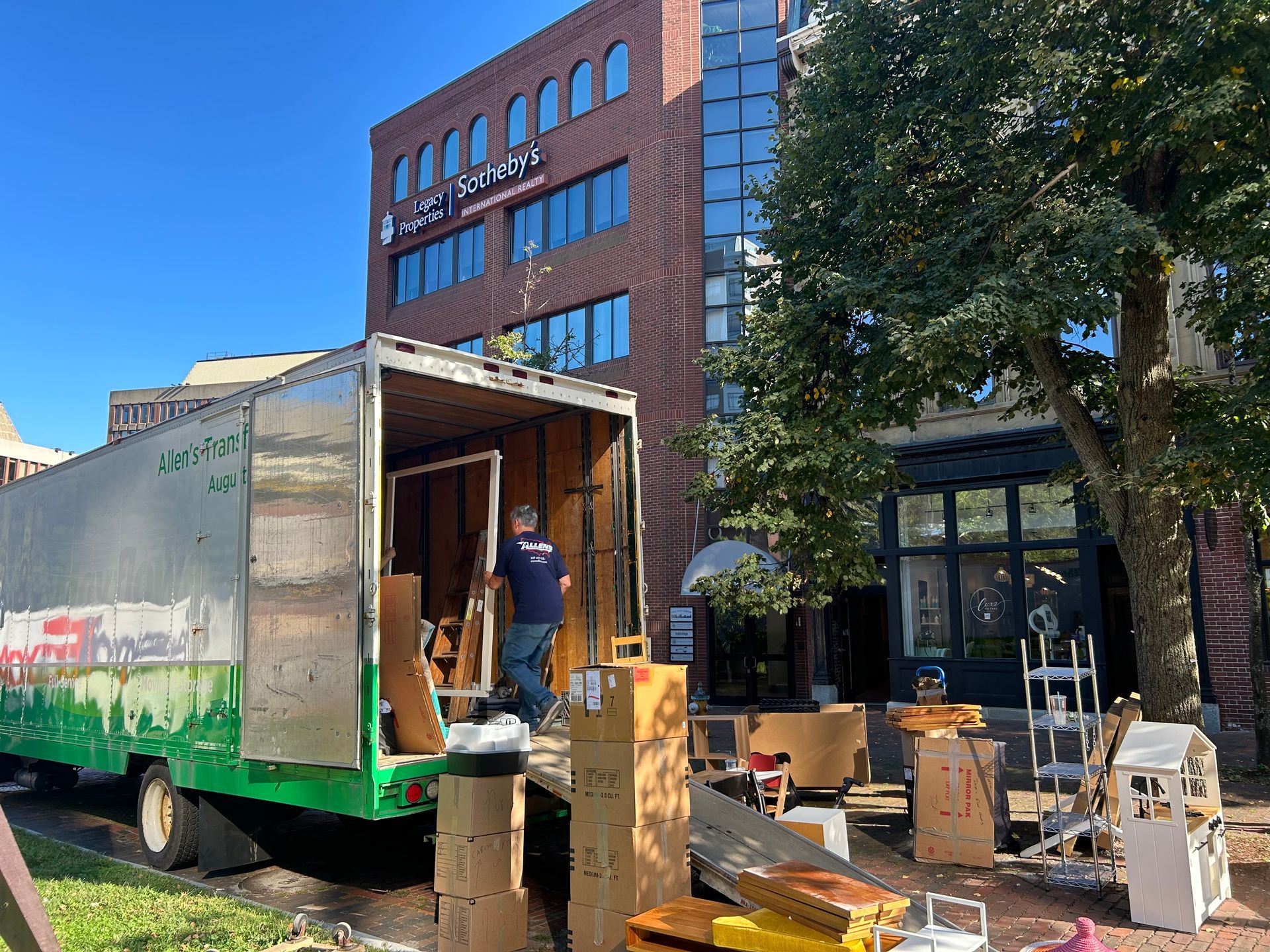 A green and white moving truck is parked in front of a large building.