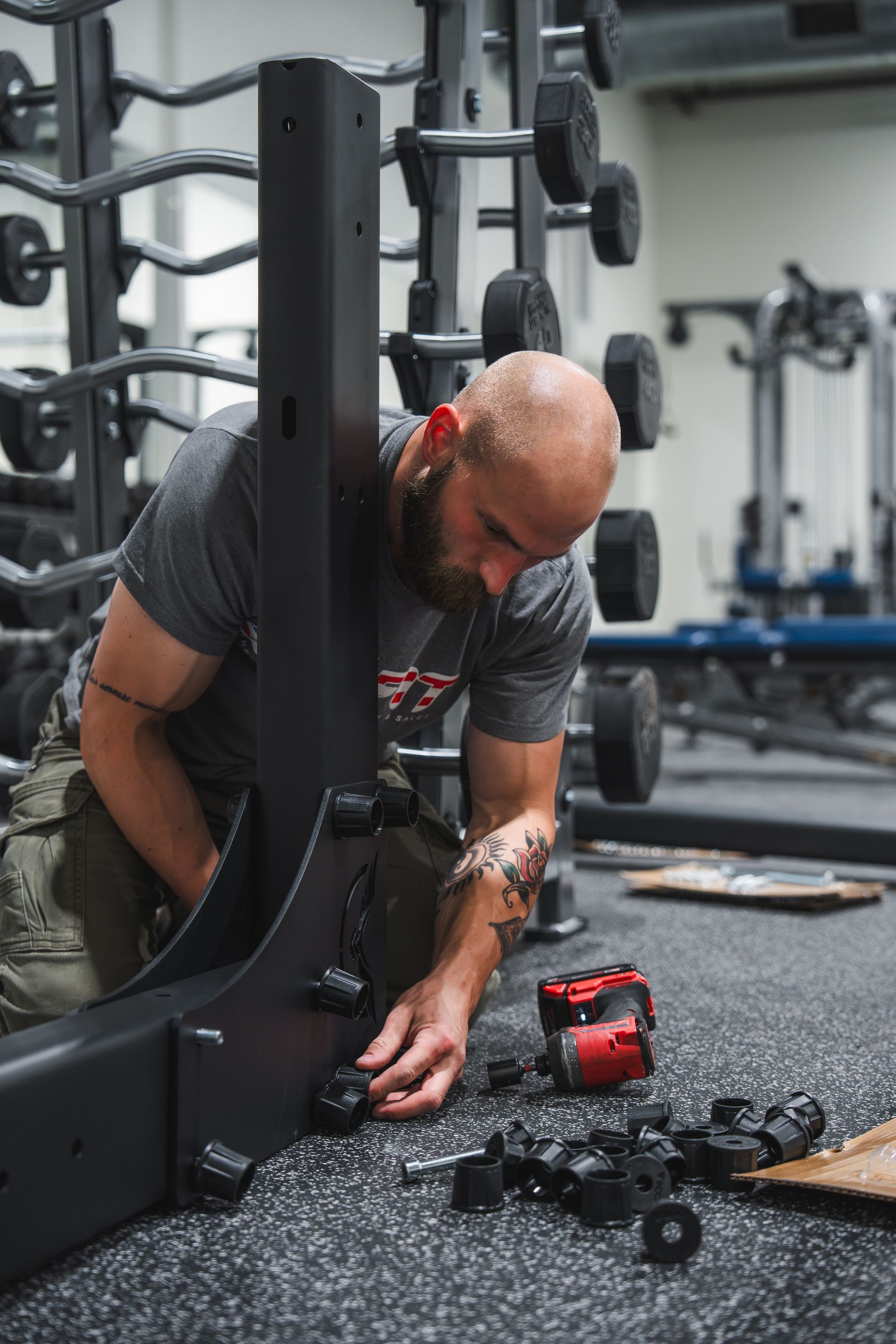 Man repairing elliptical machine in a gym, with tools scattered nearby.