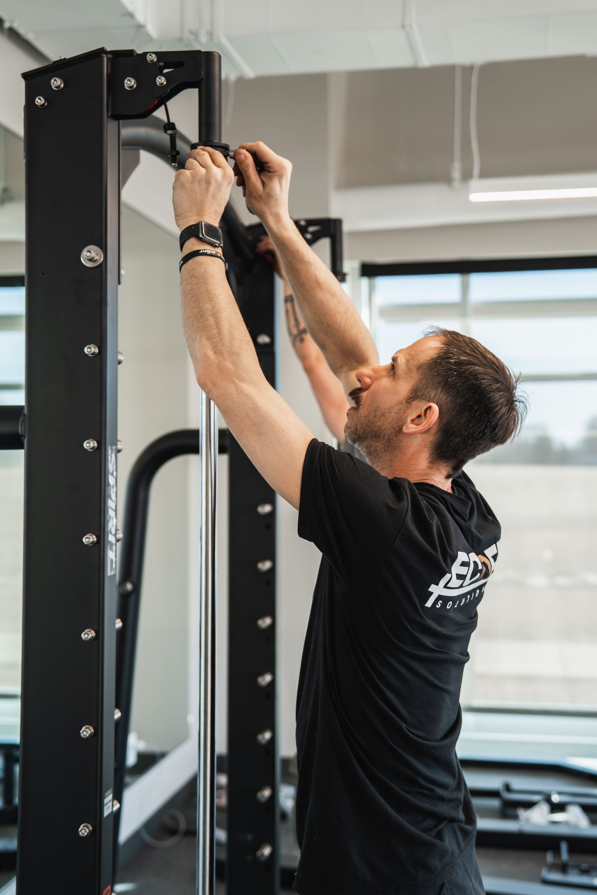 Person adjusting a cable machine in a gym while holding a clipboard