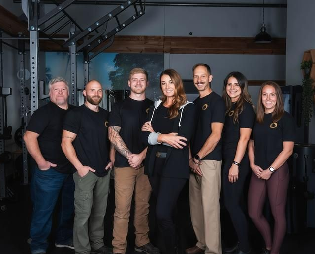Group of seven people, likely fitness professionals, in a gym. All are wearing black shirts.