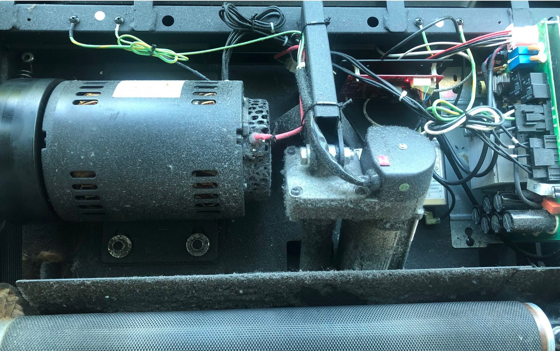 Inside view of a dusty treadmill showing the motor, circuit boards, and other mechanical components.