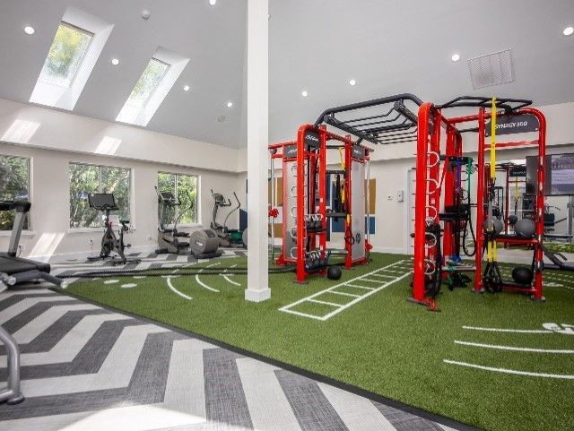 Gym with red workout equipment, green turf, chevron flooring, and skylights.