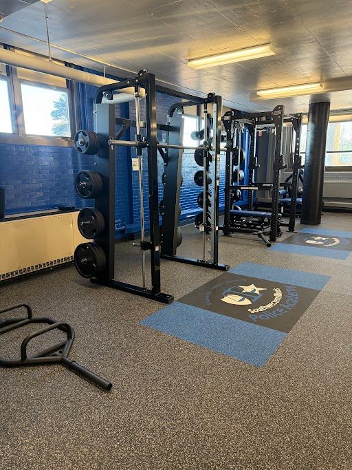 Gym interior with exercise equipment on a speckled floor, including treadmills, rowers, and ellipticals.