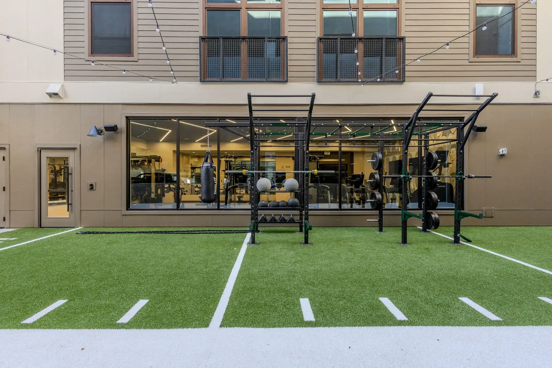 Outdoor gym with pull-up rack on artificial turf in front of a glass-walled building
