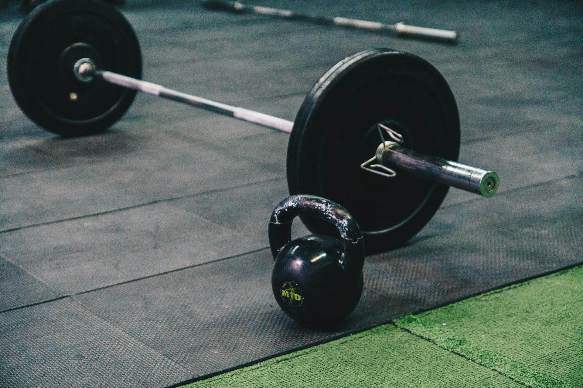Barbell and kettlebell on a gym floor with green turf edge