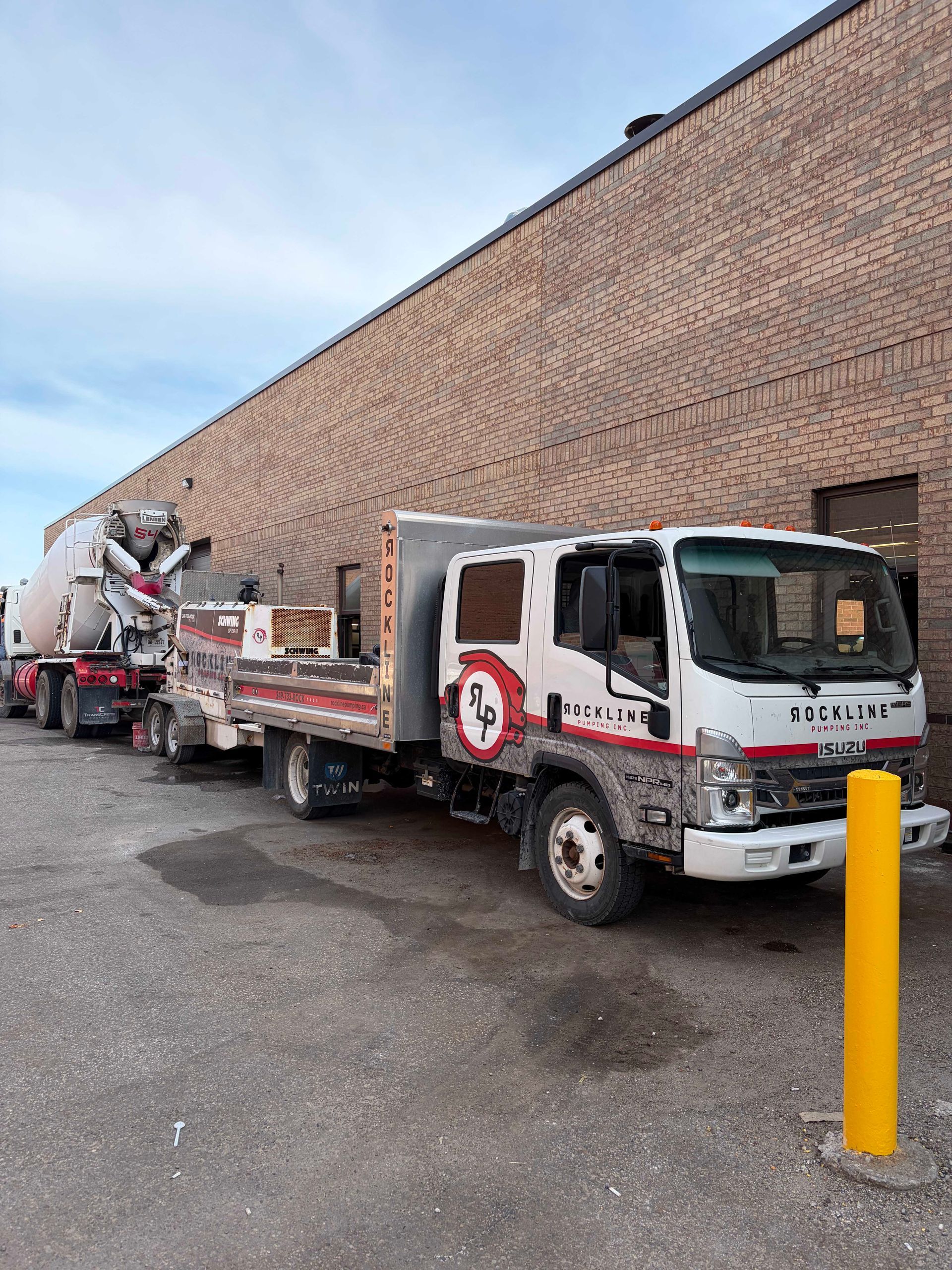 White utility truck with cement mixer parked beside a brick building in an industrial lot.