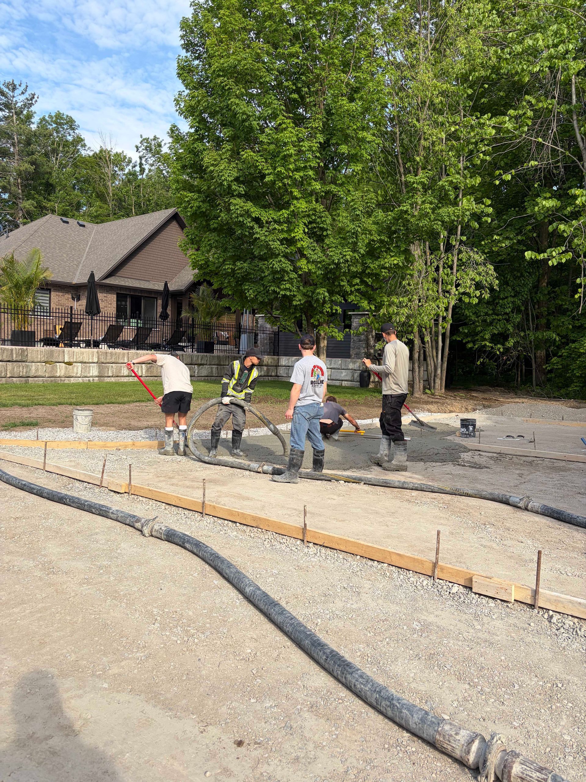 People working on a curved gravel path beside a wooded area and a rustic building.