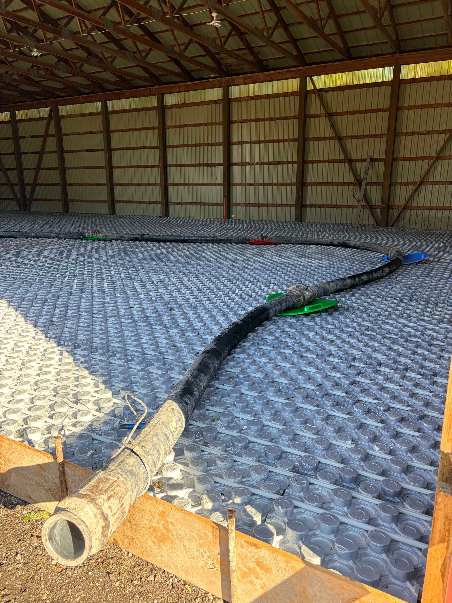 Large empty barn with a patterned floor mat and a black hose or cable stretched across it