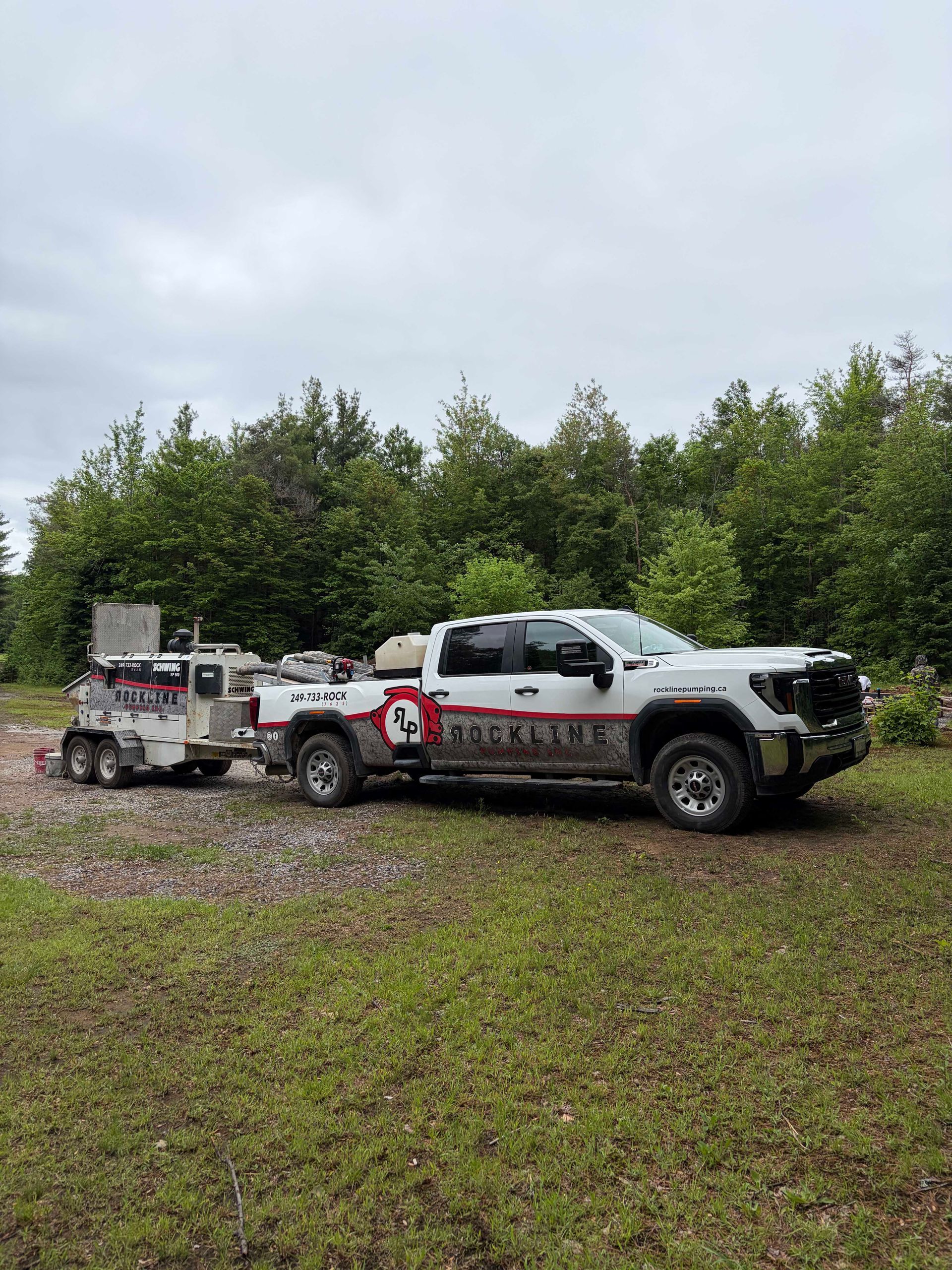 Two white pickup trucks with off-road gear parked on grass in front of trees under a cloudy sky