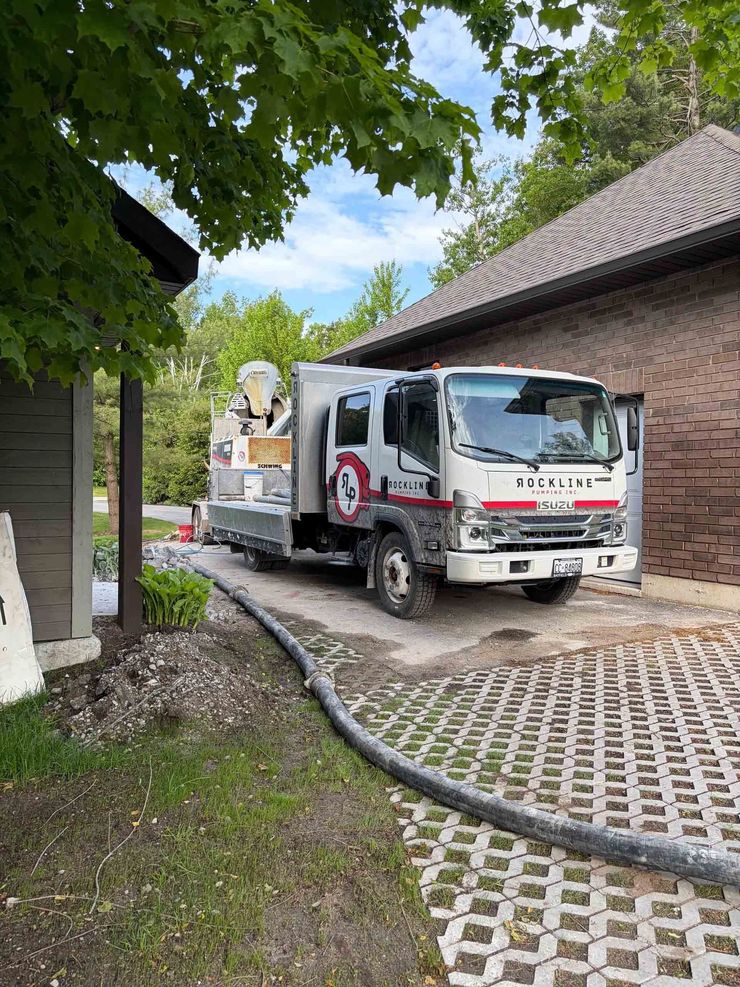 Red-and-white utility truck parked on a cobblestone driveway beside a house, under leafy trees.