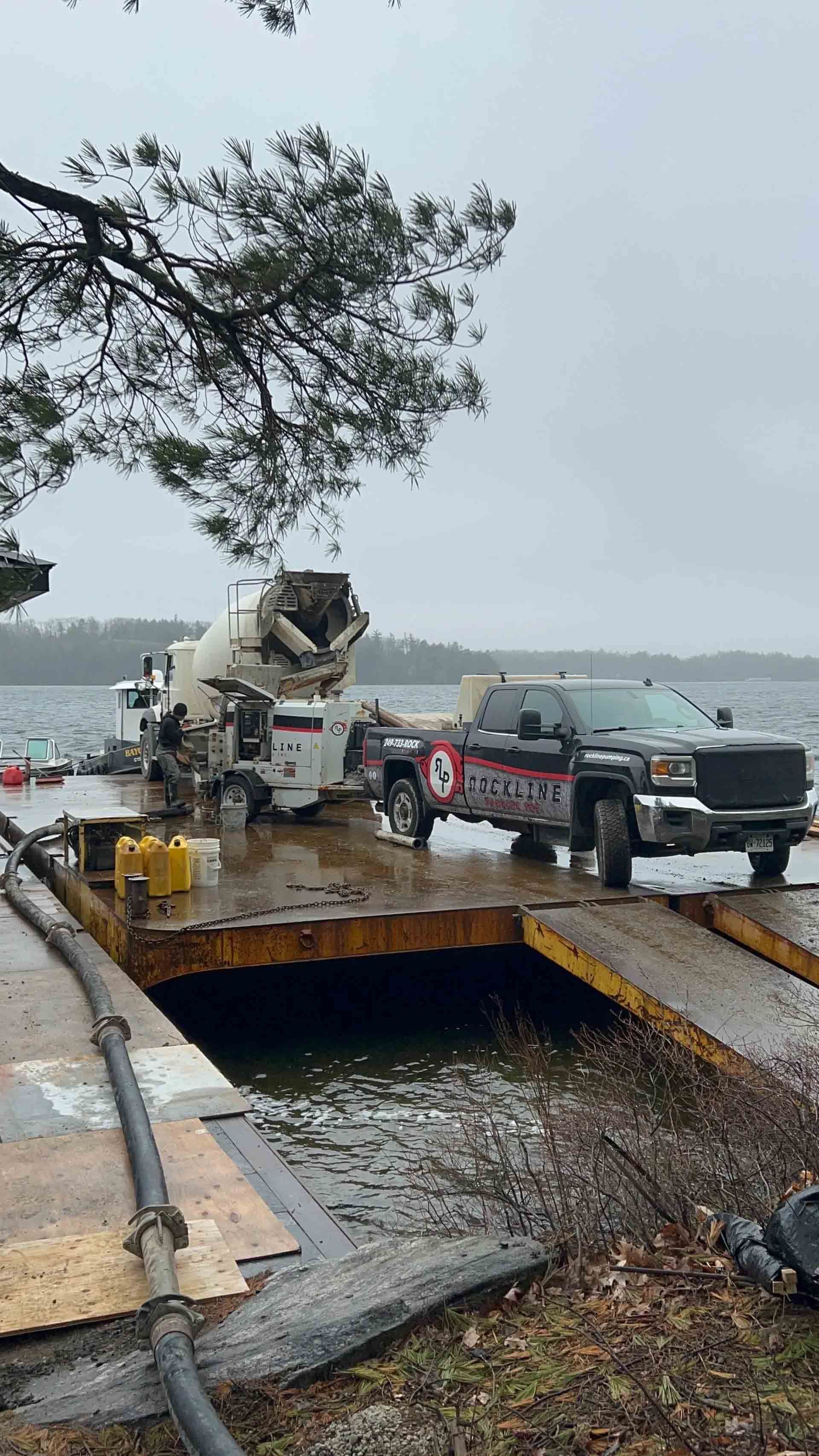 Tow truck lifting a black pickup from a flooded roadside near the water under gray skies