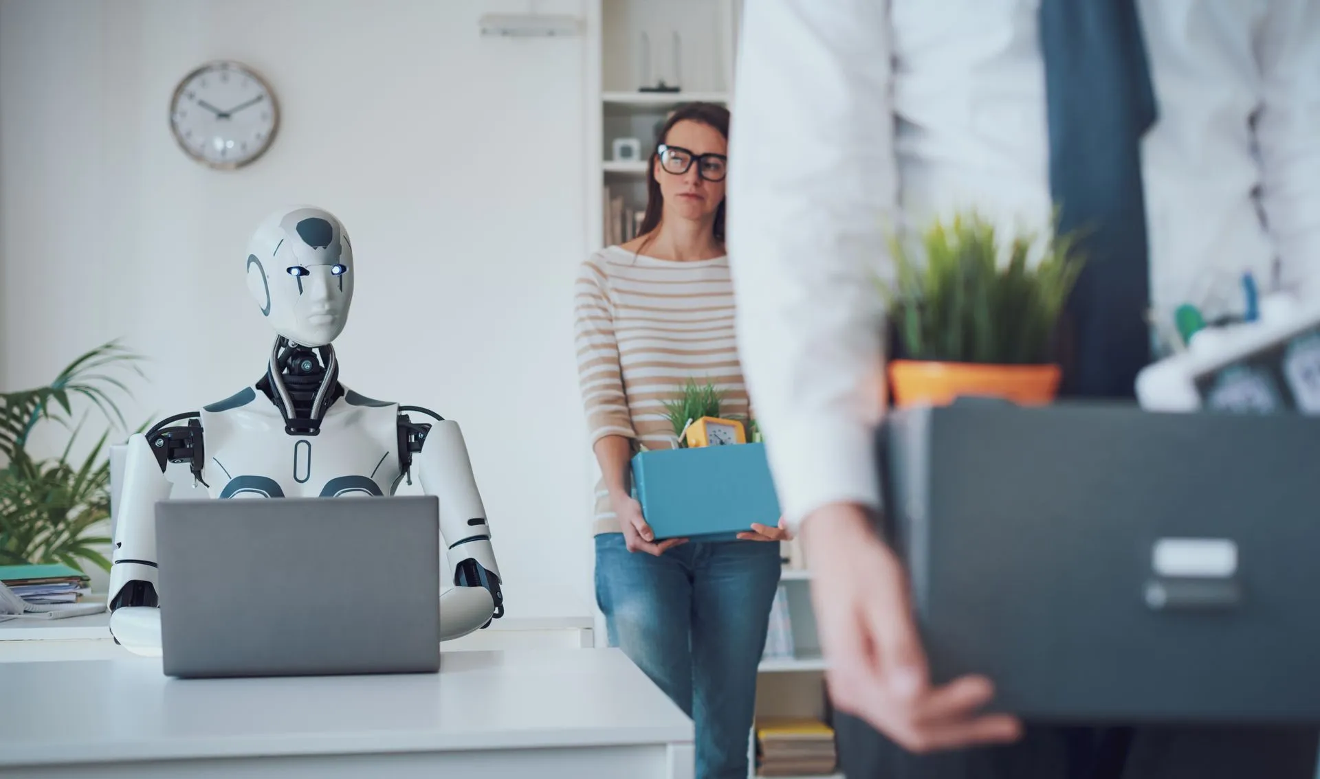 A robot on a computer in an office watching people walking out,carrying their belongings in boxes