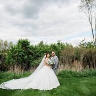 Bride and groom in wedding attire posing on a grassy lawn with lush greenery behind them