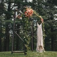 White dress hanging from a tree branch beside orange flowers in a wooded clearing