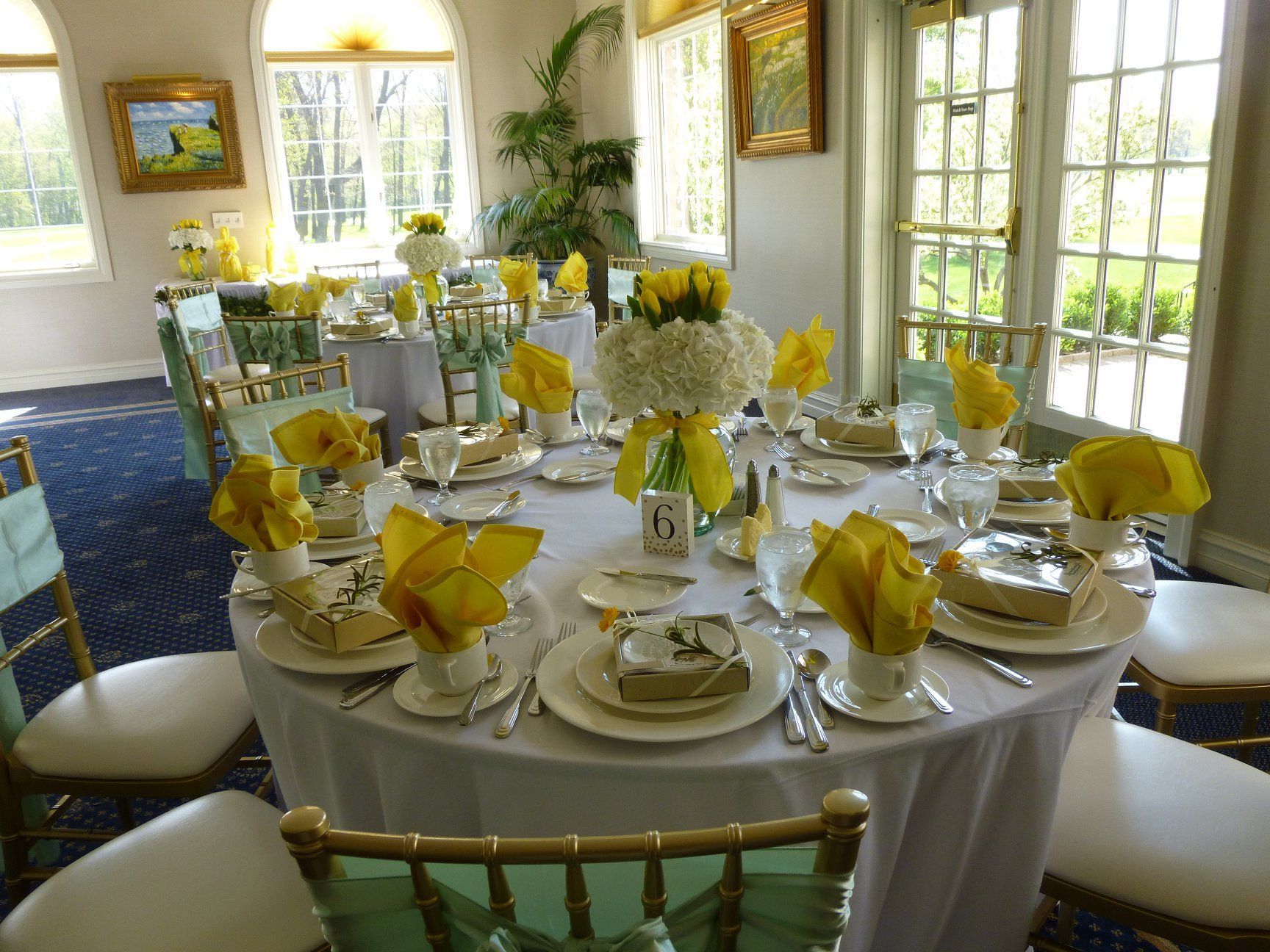 Elegant dining room with round tables set for a formal meal, yellow napkins, and floral centerpieces.