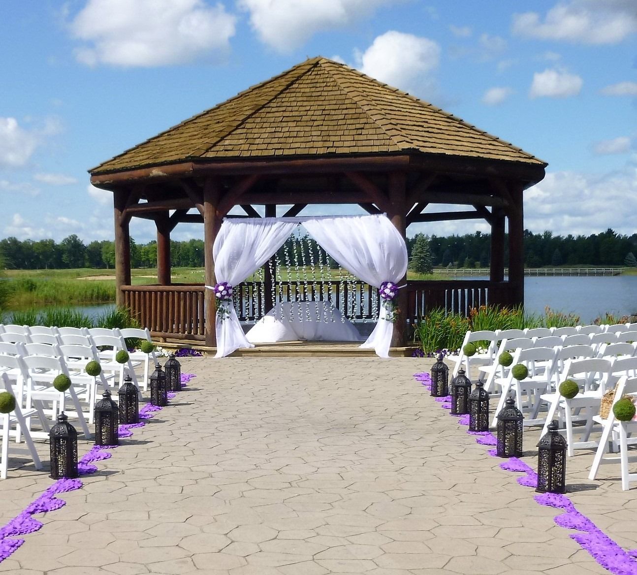 Outdoor wedding gazebo with white chairs lining a path beside a lake