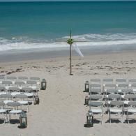 Beach wedding setup with white chairs facing the ocean and an arch on the sand