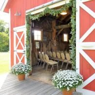 Open red barn entrance with chairs inside and white flowers in pots at the doorway