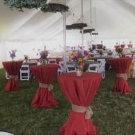 Round tables with red tablecloths and floral centerpieces inside a white event tent