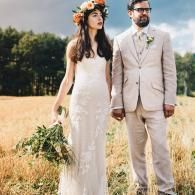 Bride and groom standing in a wheat field, bride in a white dress and flower crown, groom in a beige suit