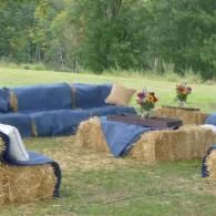Hay bale seating with blue covers and flower centerpieces outdoors on grass