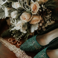Green shoes beside a bouquet of cream roses and a beaded clutch on a textured rug