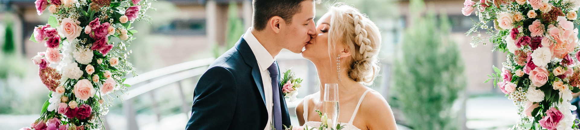 Bride and groom kissing under pink and white floral arch at outdoor wedding ceremony