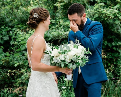Bride and groom in blue suit share an emotional moment outdoors, holding white flowers