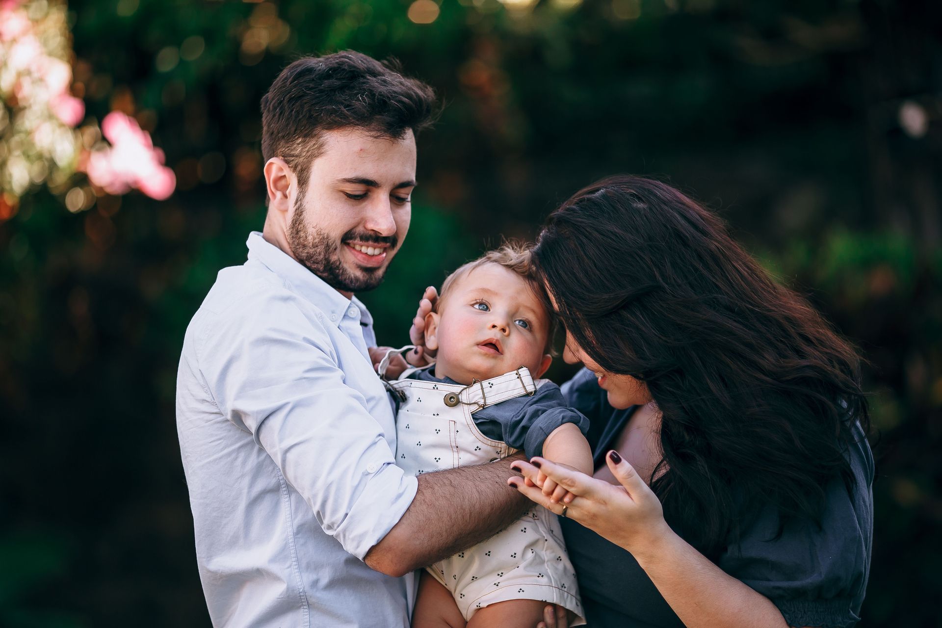 Smiling couple holding a baby outdoors in a green, softly blurred setting