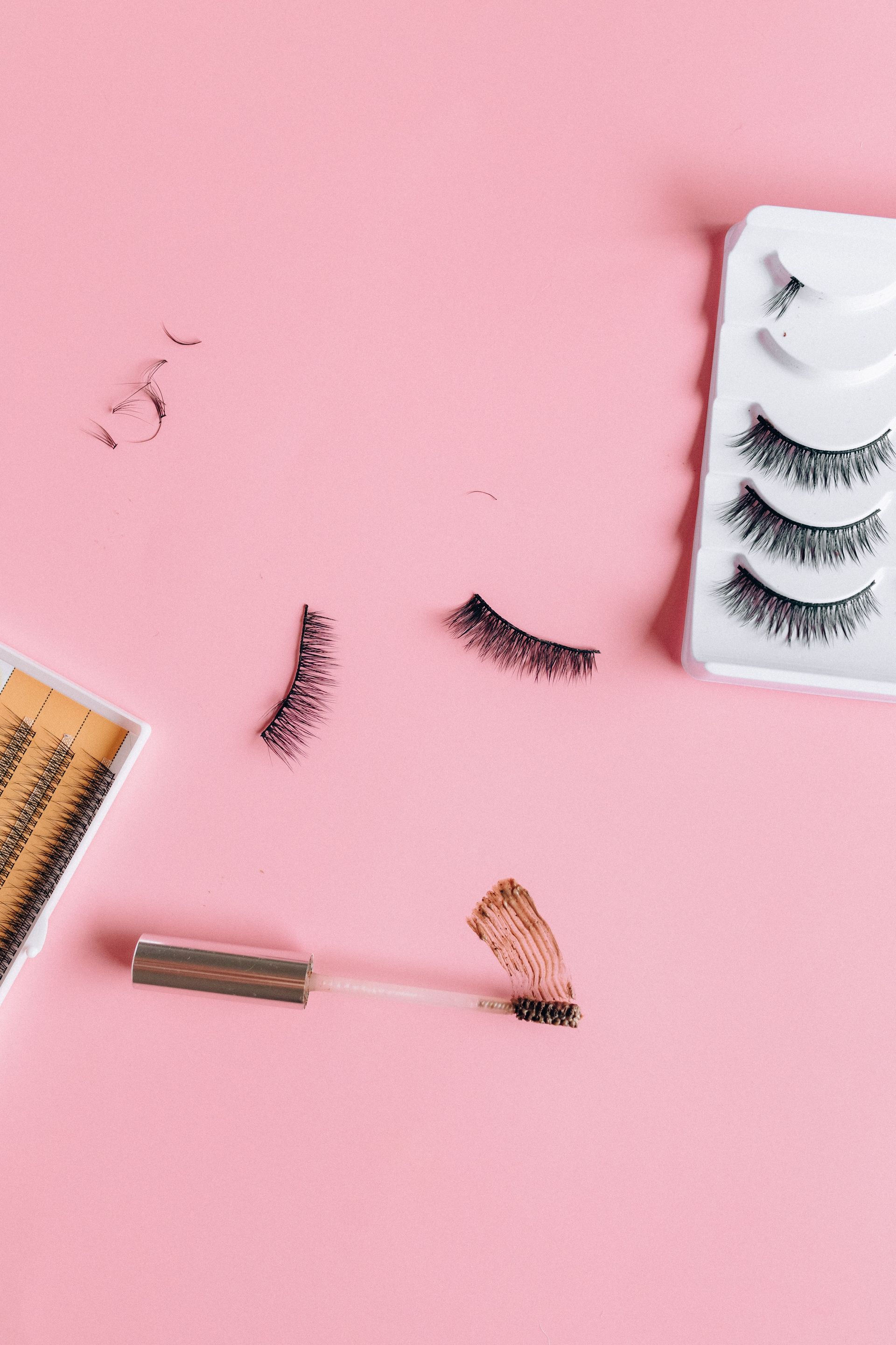 False eyelashes, mascara wand, and makeup tools on a pink background