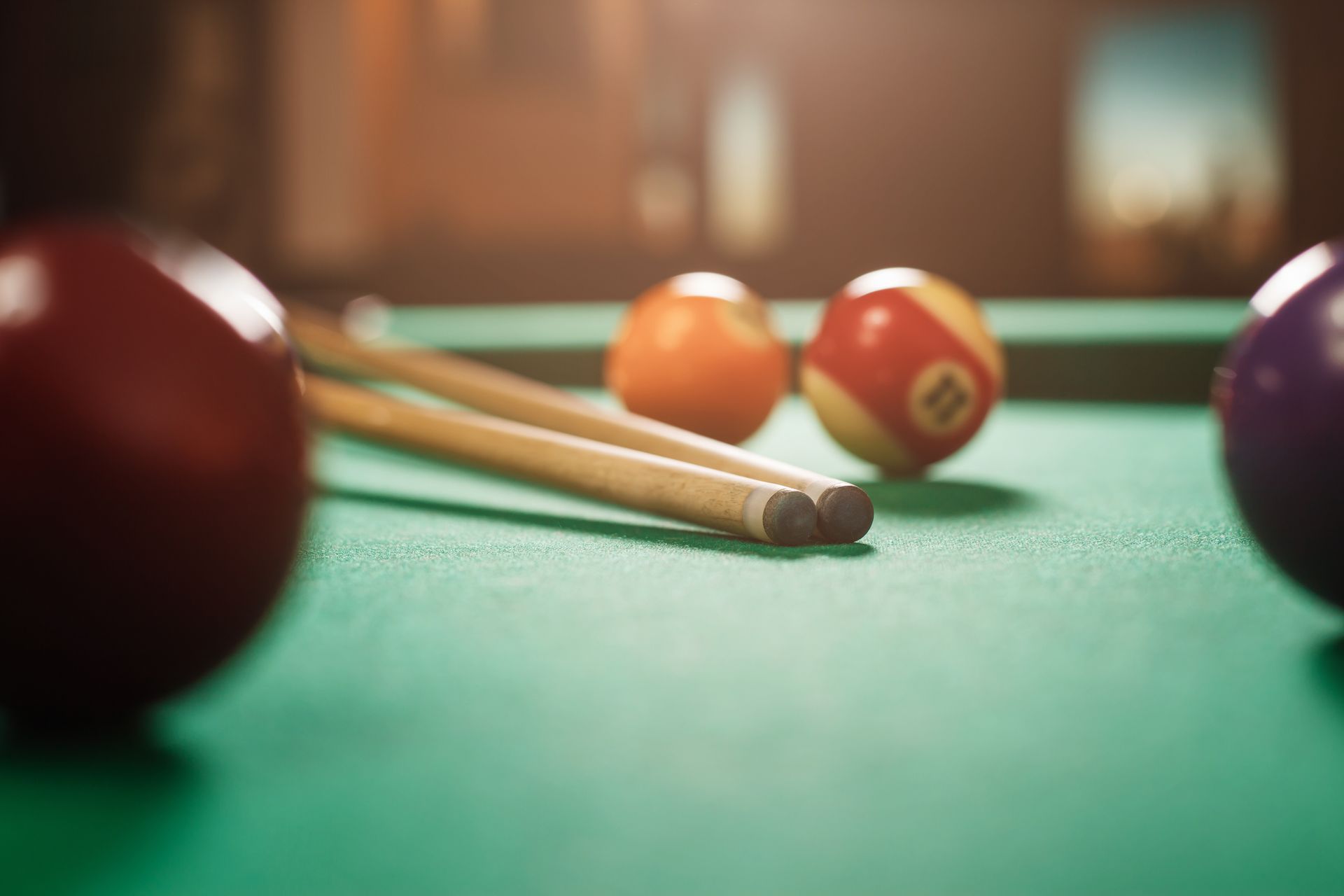Billiards table with green felt, cue sticks, and several balls in soft focus